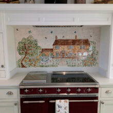 Hand painted tile mural of house and tree behind range cooker